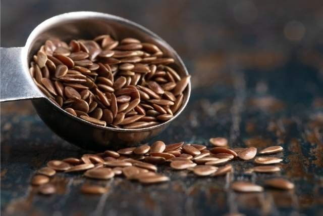 Metalllöffel voller Leinsamen auf dunklem Tisch für das selber machen von Leinsamengel